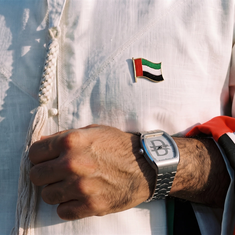 Grandeur Dirham on wrist — kandura with UAE flag